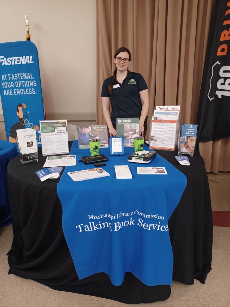 Megan standing behind the Talking Book Services booth.