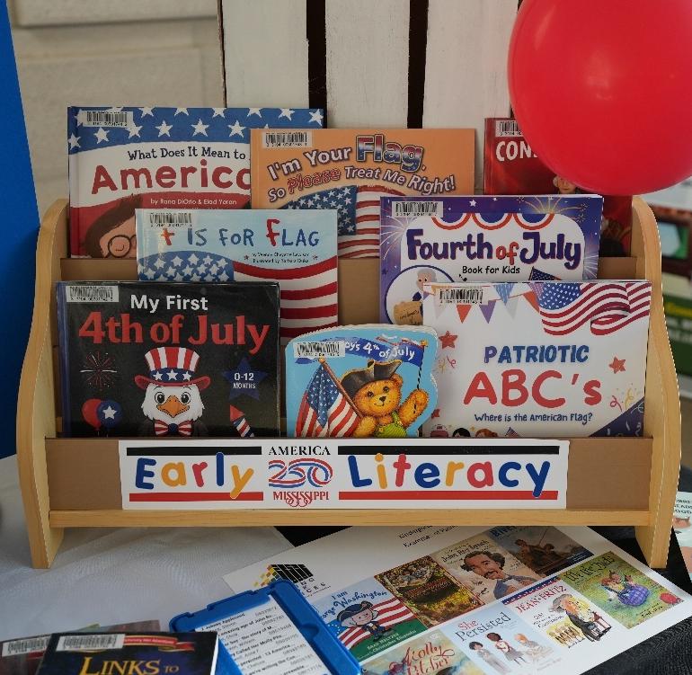 Wooden display rack labeled ‘Early Literacy’ holding children’s books about America, flags, and the Fourth of July, with a red balloon on the side.