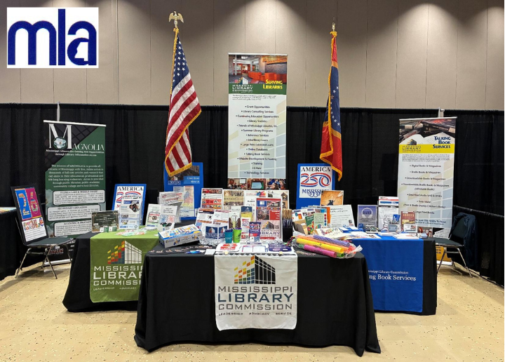 Mississippi Library Commission booth with America 250 signage, U.S. and state flags, books, and informational banners displayed at an event with the MLA logo in the background.