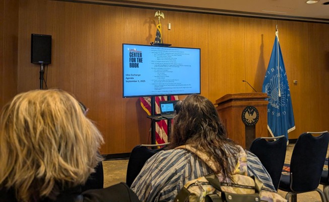 Presentation room with a wooden podium, U.S. and Smithsonian flags, and a screen displaying ‘Center for the Book’ agenda for September 6, 2025.