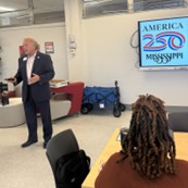 Marvin Jeter presents in front of a screen with the text “America 250 Mississippi.”