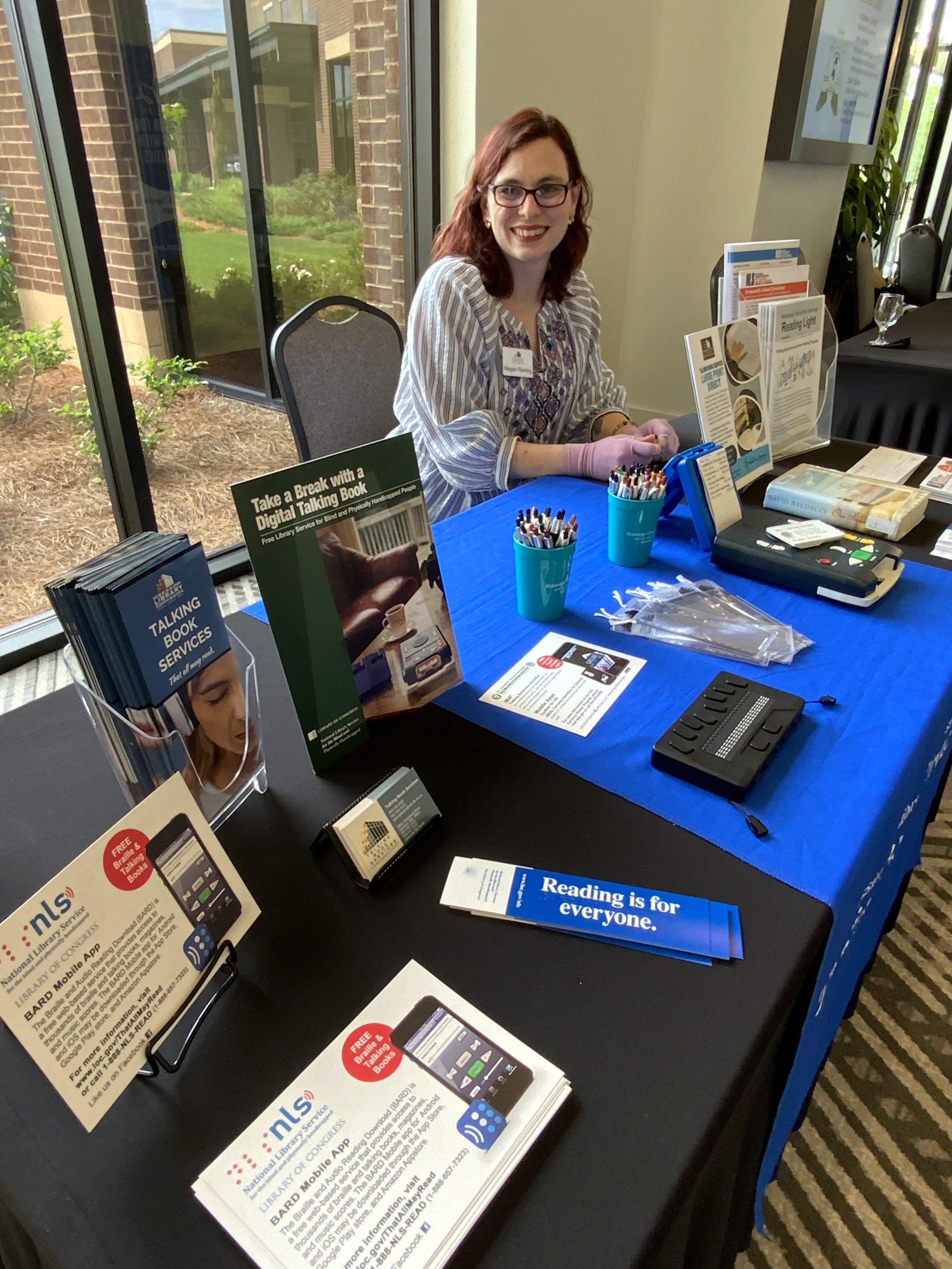 A display table with brochures, devices, and promotional materials for accessible library services at Health Aging MS Conference.