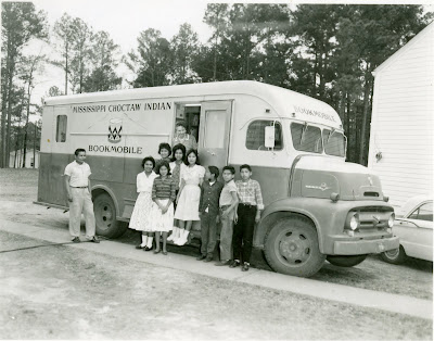 Black and white photo of the Mississippi Choctaw Indian bookmobile with a group of children standing beside it.